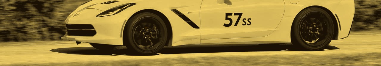 A yellow Chevrolet Corvette at speed on an autocross course, driver in a red helmet